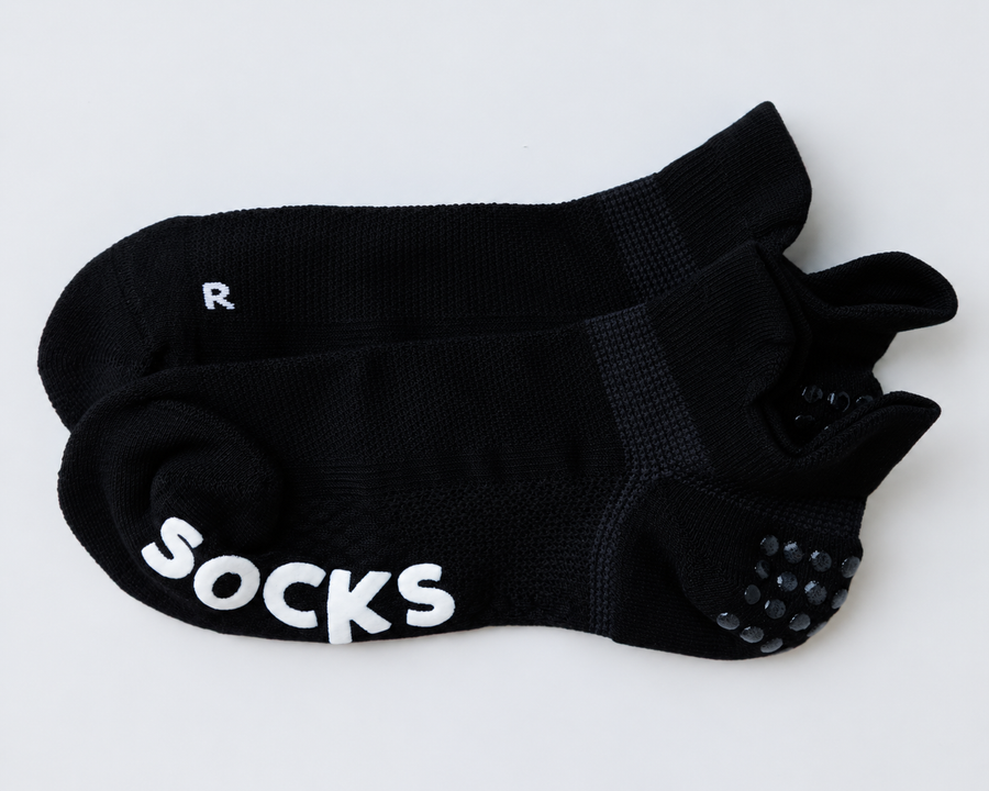 One pair of black ankle grip socks laid together, showing heel tabs, grip dots, and a right-foot marking. By Squid Socks.