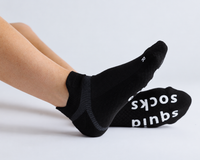 Thumbnail for Black ankle grip socks worn with legs extended, showing top and sole views. By Squid Socks.