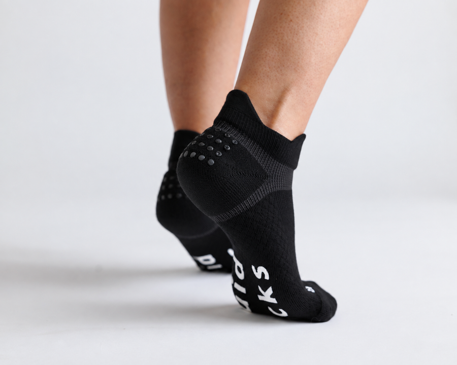 Black ankle grip socks viewed from behind with heels raised, showing heel and bottom grips. By Squid Socks.