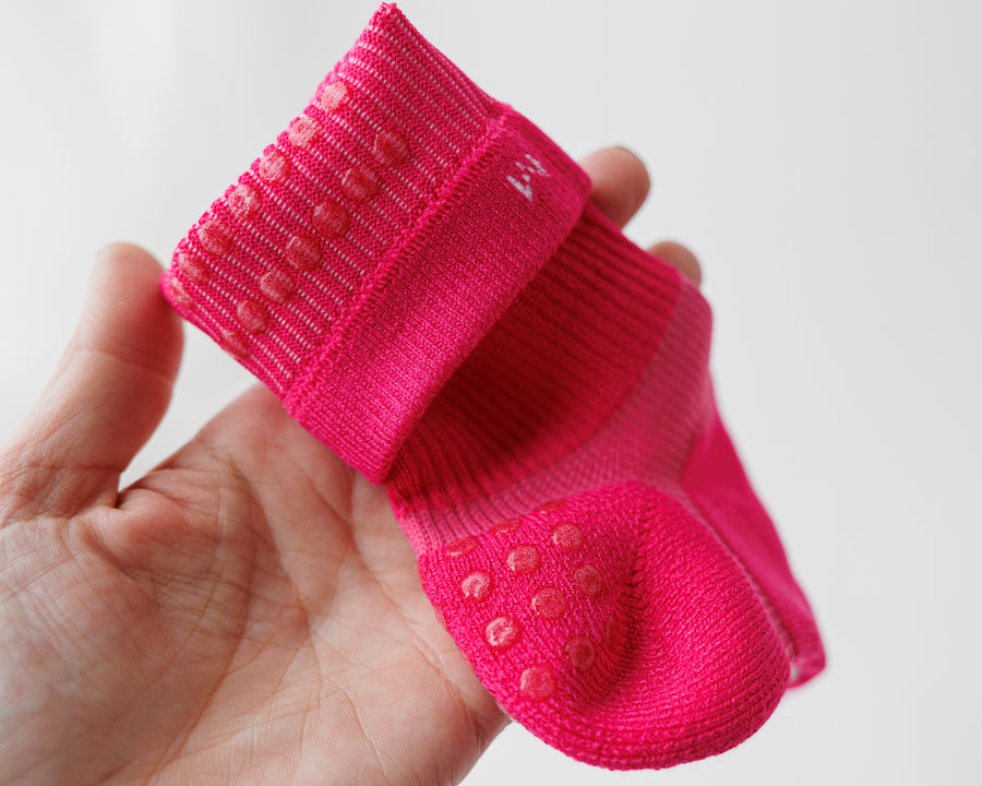 Hand holding an Electric Pink crew sock with the cuff folded back, showing cuff and heel grip dots. By Squid Socks.