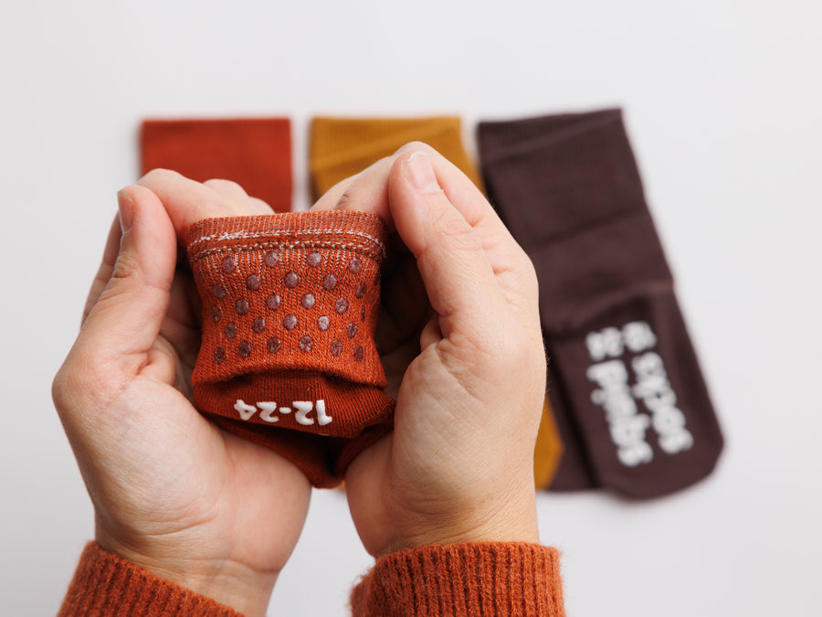 Cedar kids socks: hands holding a rust sock to show cuff grip dots. Squid Socks, the brand seen on Shark Tank.