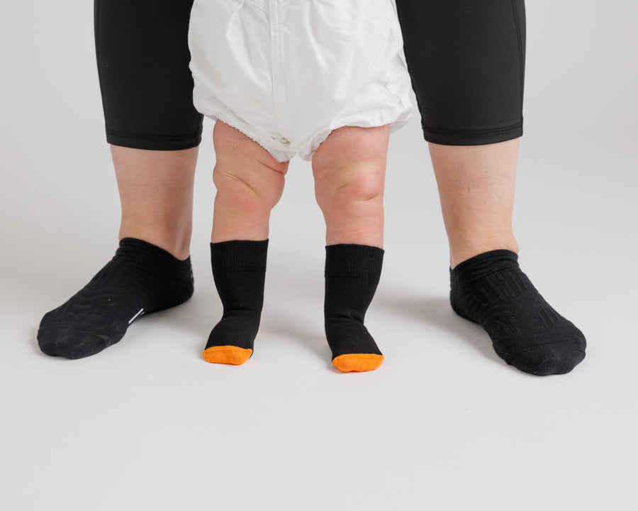 Child standing beside an adult wearing Candy Corn grip socks with orange toes.