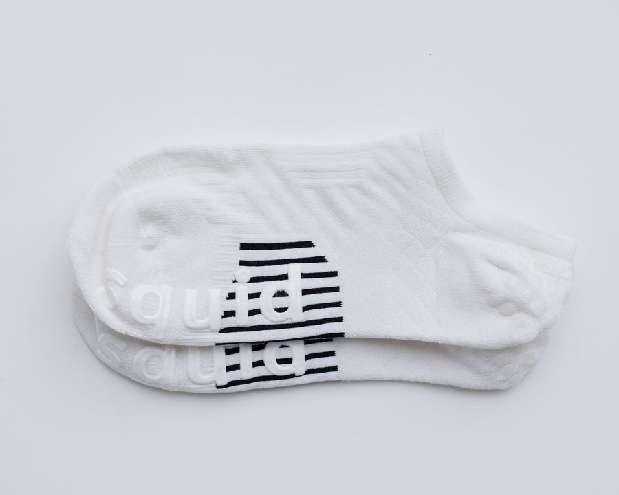 One pair of white no-show grip socks laid together, showing black bottom grips. By Squid Socks.