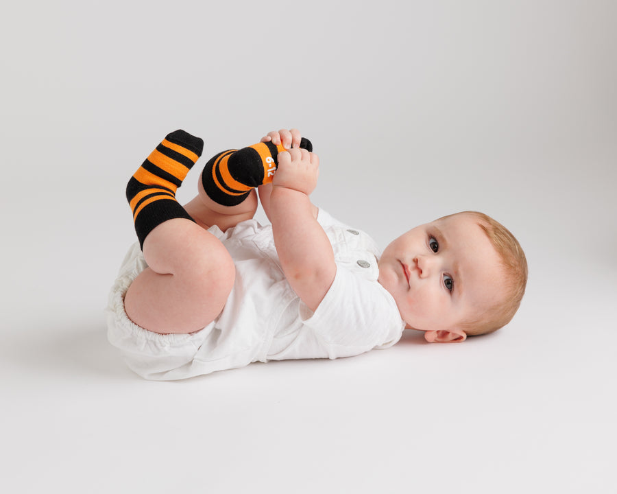 Baby lying down wearing black and orange striped Candy Corn grip socks.