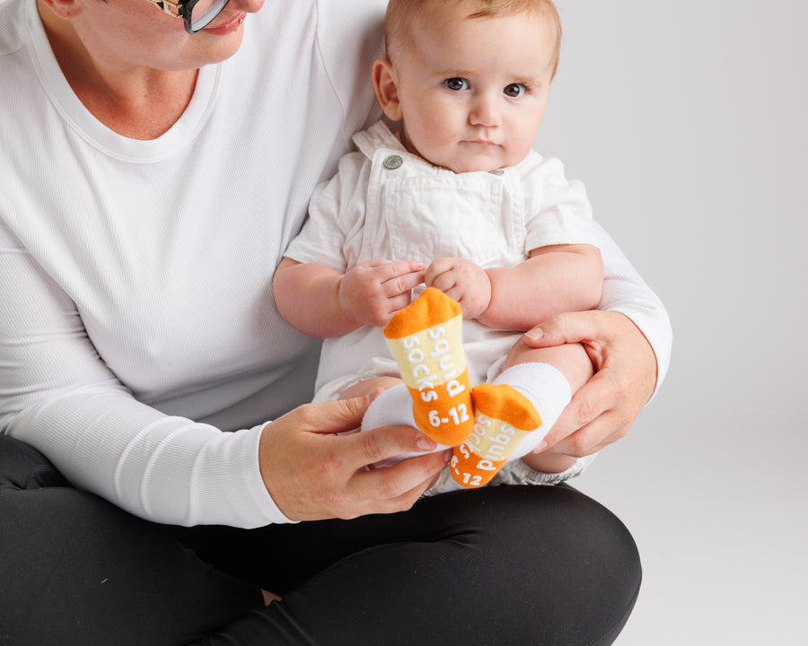 Adult holding a baby wearing white, orange and yellow Candy Corn grip socks.