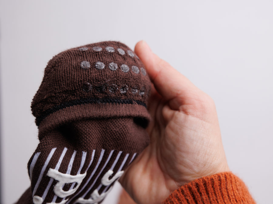Close-up of a brown no-show sock heel held in one hand, showing rows of grip dots. By Squid Socks.