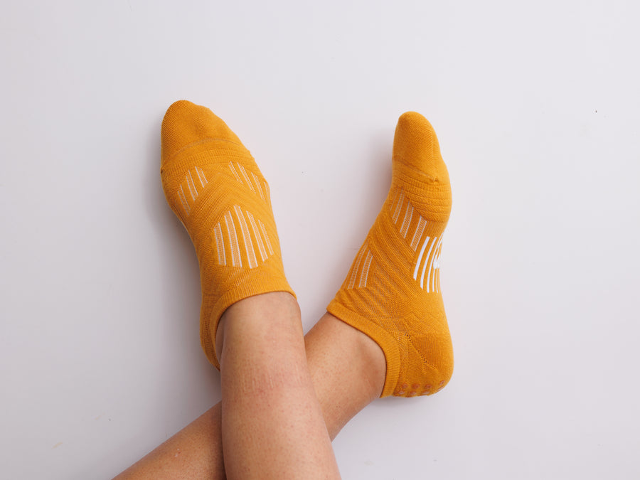 Mustard yellow no-show grip socks worn with ankles crossed, viewed from above. By Squid Socks.