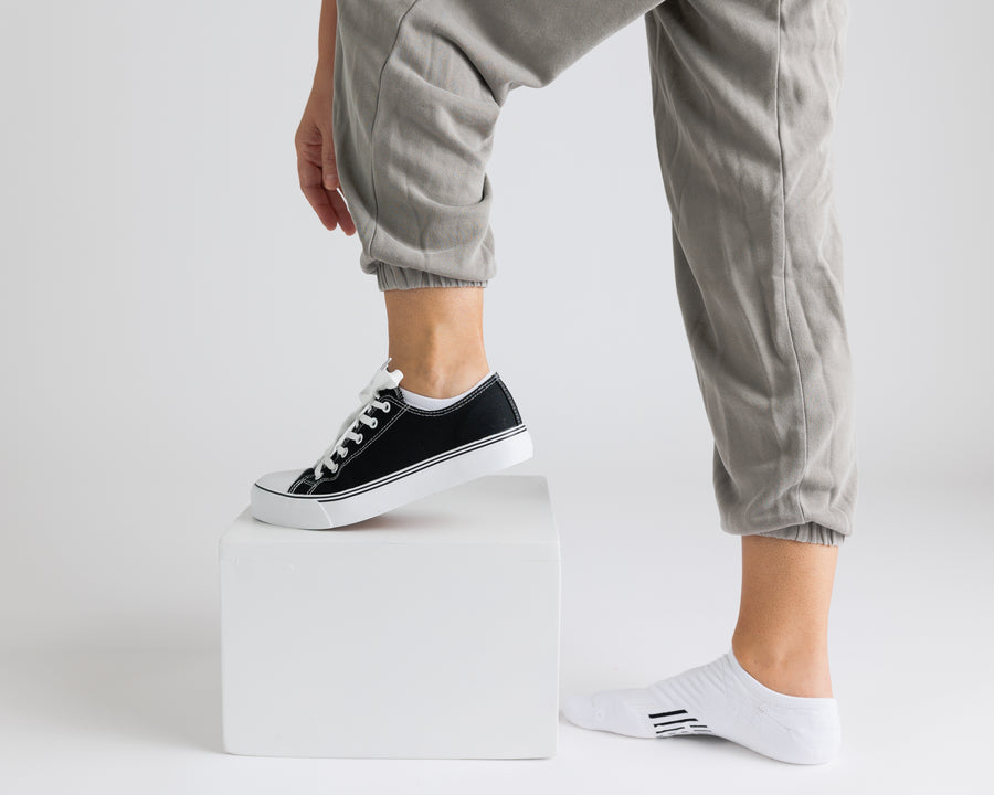 Person wearing white no-show grip socks with one black sneaker and one socked foot visible. By Squid Socks.