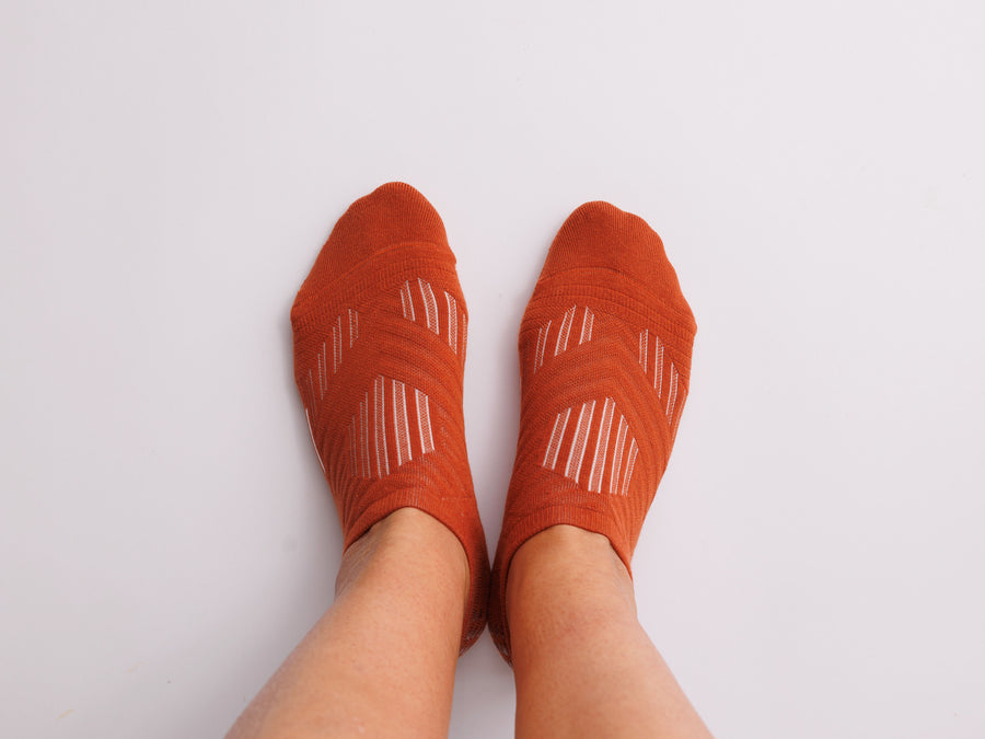 Rust orange no-show grip socks worn on both feet, viewed from above. By Squid Socks.