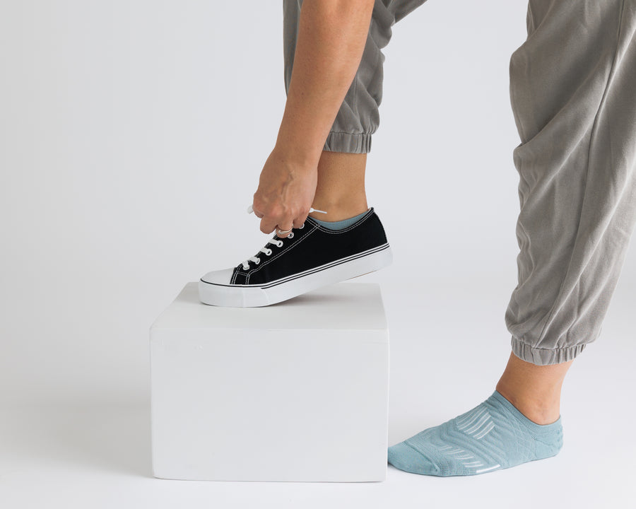 Person wearing teal no-show grip socks while putting on a black sneaker. By Squid Socks.