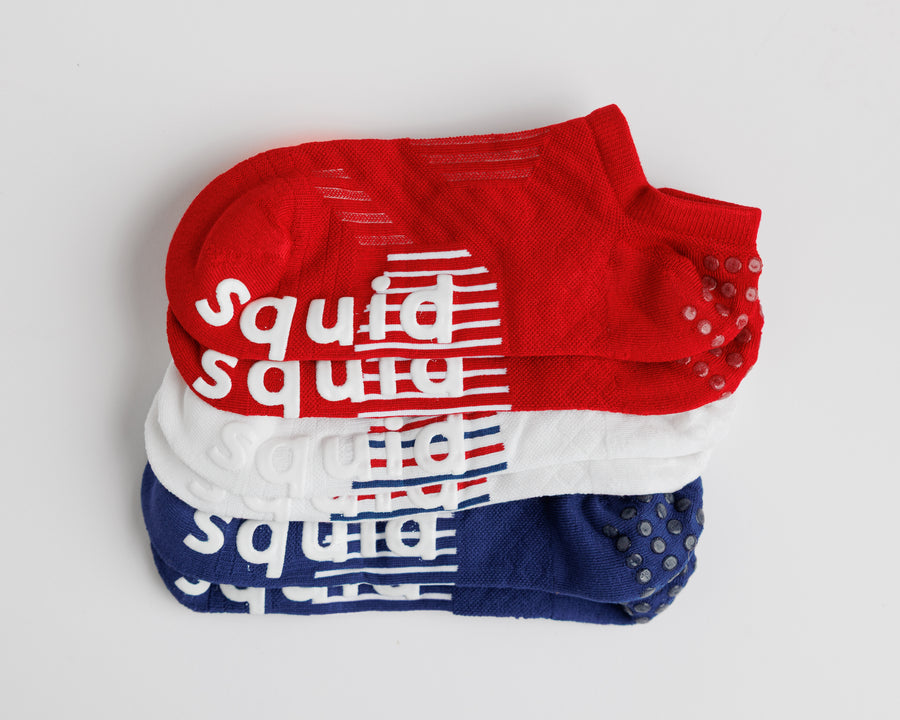 All-American no-show grip socks in red, white, and navy, stacked with bottom grips visible. By Squid Socks.