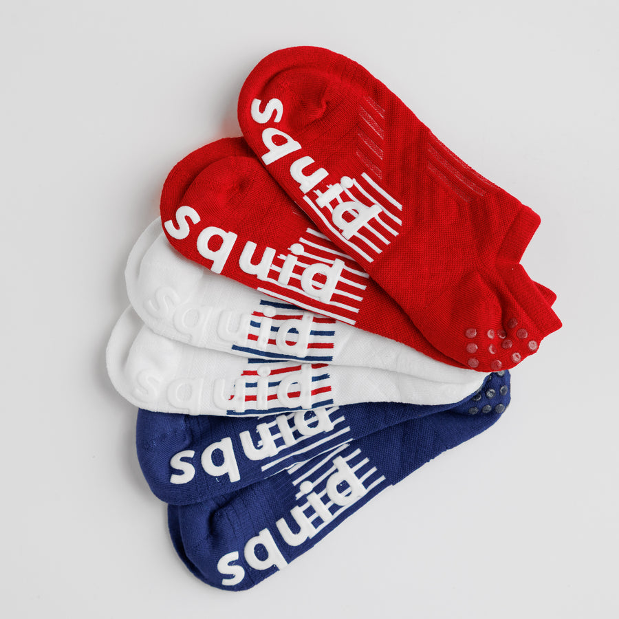 Red, white, and navy All-American no-show grip socks arranged to show the striped bottom grips. By Squid Socks.