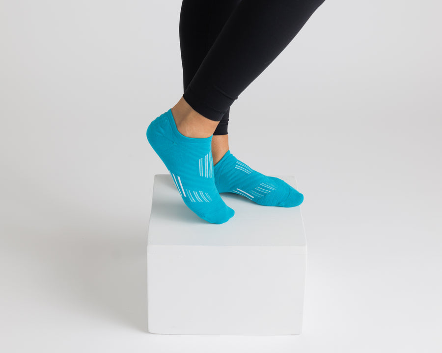 Turquoise no-show grip socks worn with black leggings on a display block. By Squid Socks.