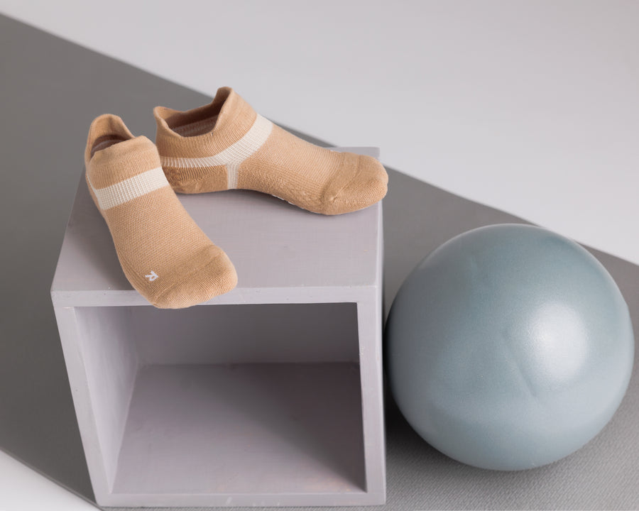 Tan ankle grip socks displayed on a cube beside an exercise ball. By Squid Socks.