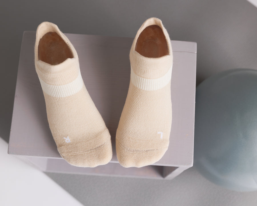 Cream ankle grip socks displayed from above beside an exercise ball. By Squid Socks.