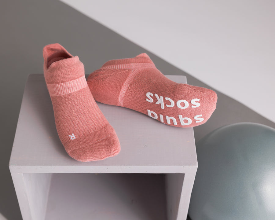 Coral ankle grip socks displayed on a cube, showing top and sole views. By Squid Socks.