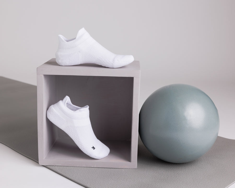 White ankle grip socks displayed on a cube beside an exercise ball. By Squid Socks.