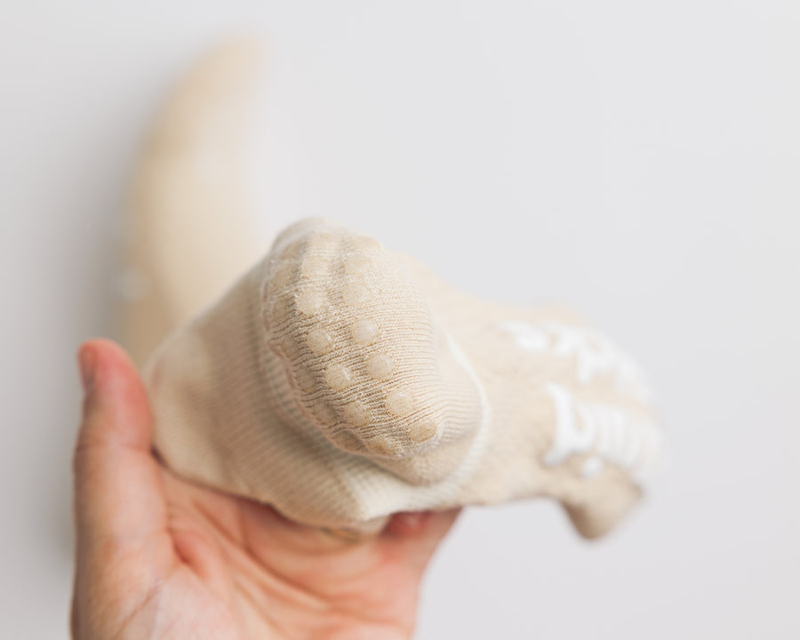 Close-up of a cream ankle sock held in one hand, showing the rounded heel. By Squid Socks.