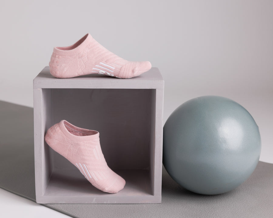 Light pink no-show grip socks displayed on a cube beside an exercise ball. By Squid Socks.