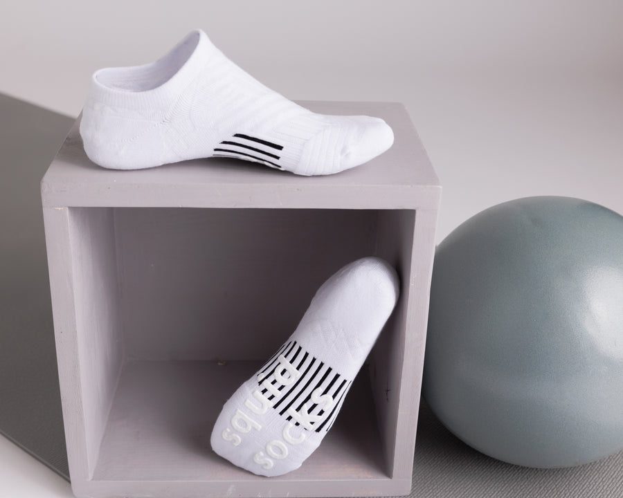 White no-show grip socks displayed on a cube, showing side and sole views. By Squid Socks.