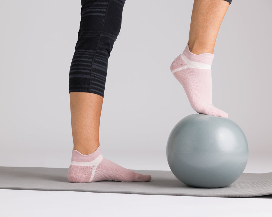 Person wearing light pink ankle grip socks with one foot resting on an exercise ball. By Squid Socks.