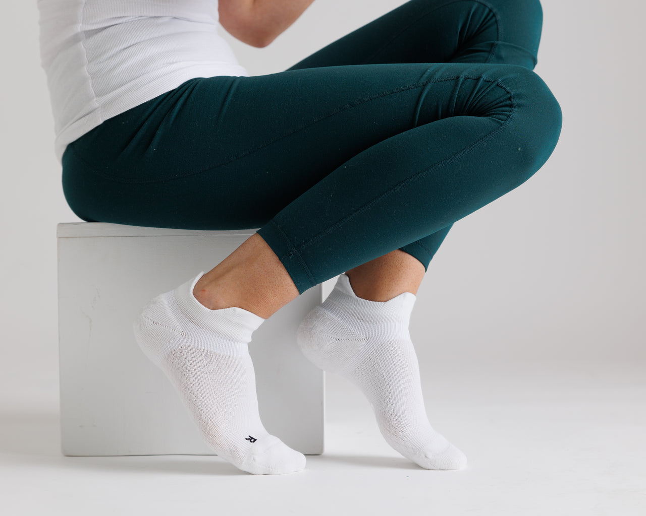 Person crouching in white ankle grip socks and teal leggings. By Squid Socks.