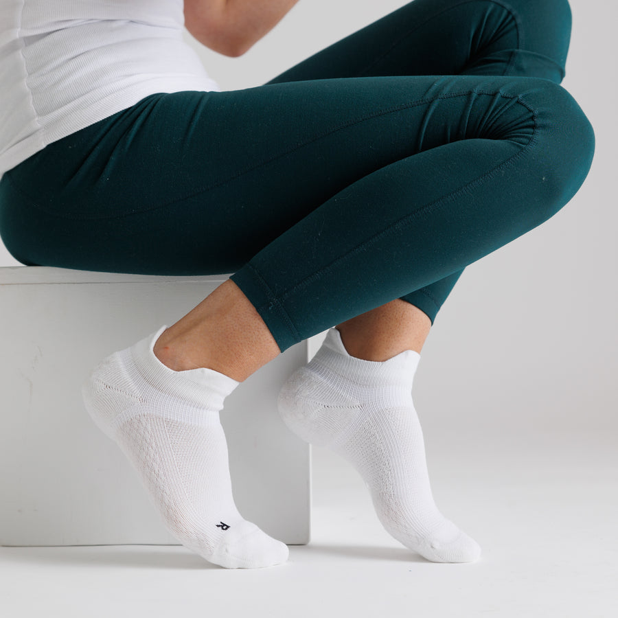 Person crouching in white ankle grip socks and teal leggings. By Squid Socks.