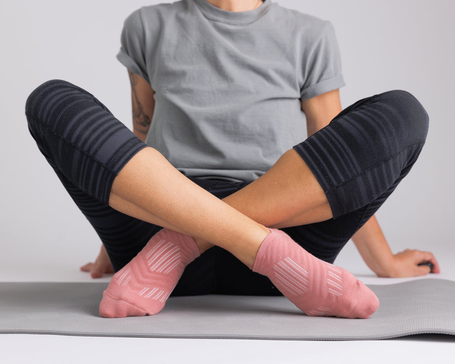 Person seated cross-legged on an exercise mat wearing coral no-show grip socks. By Squid Socks.