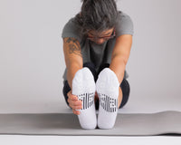 Thumbnail for Person stretching forward on an exercise mat in white no-show socks, showing black bottom grips. By Squid Socks.