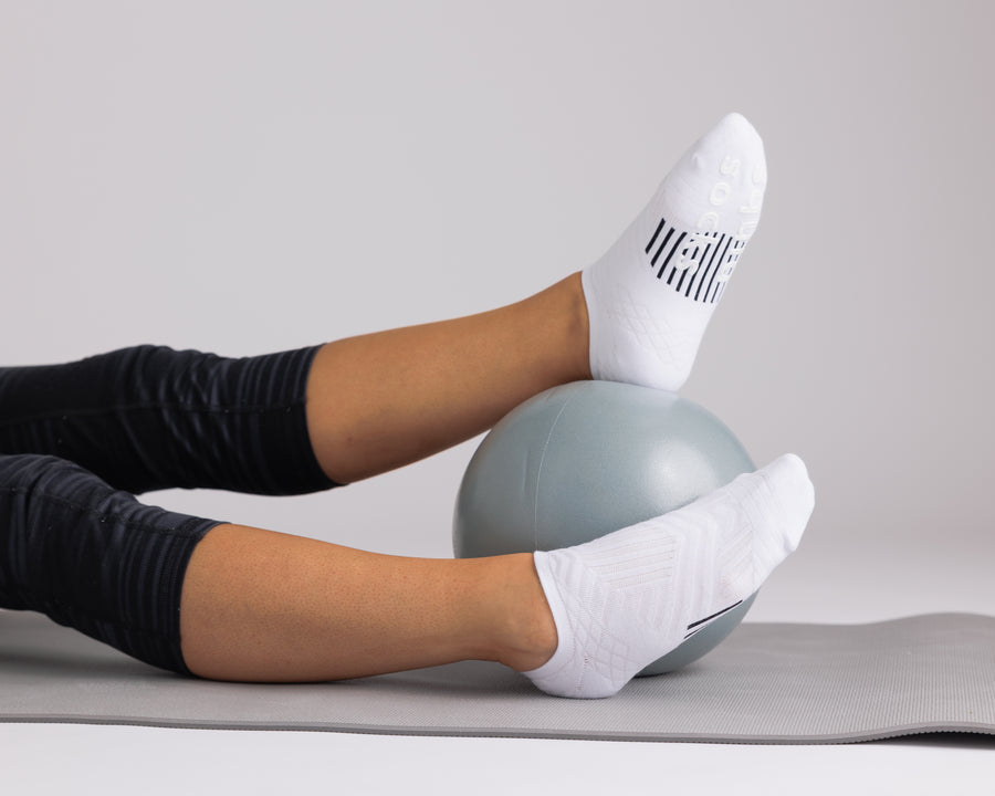 White no-show grip socks worn during a mat exercise with a small exercise ball. By Squid Socks.