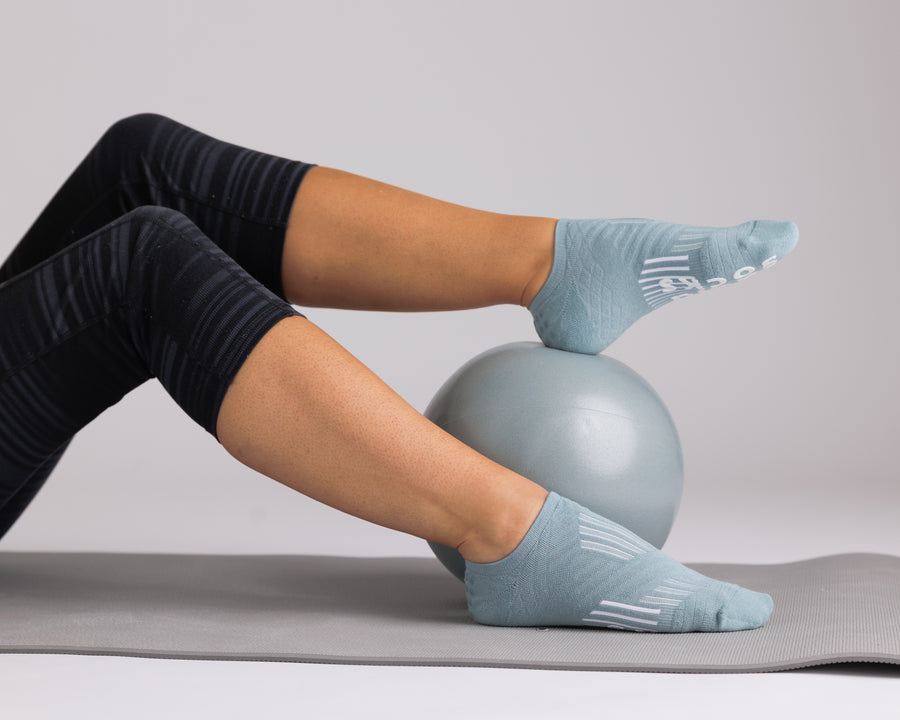 Person wearing teal no-show grip socks during a mat exercise with a small exercise ball. By Squid Socks.