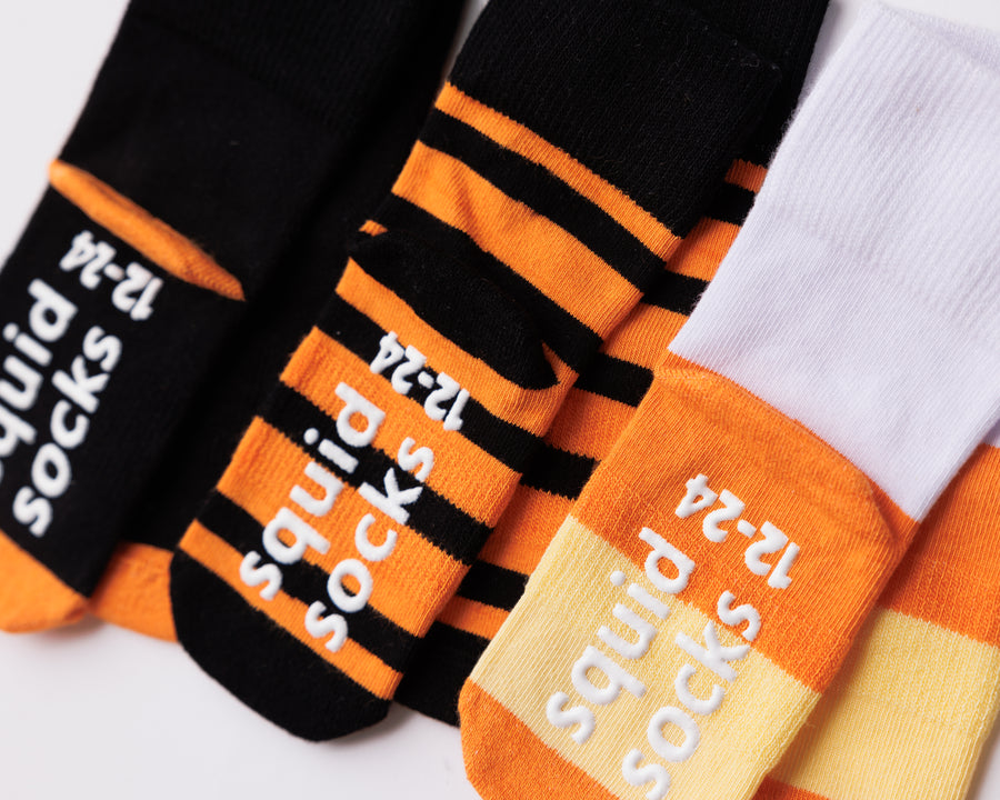 Close-up of Candy Corn socks showing orange stripes and branded silicone sole grips.
