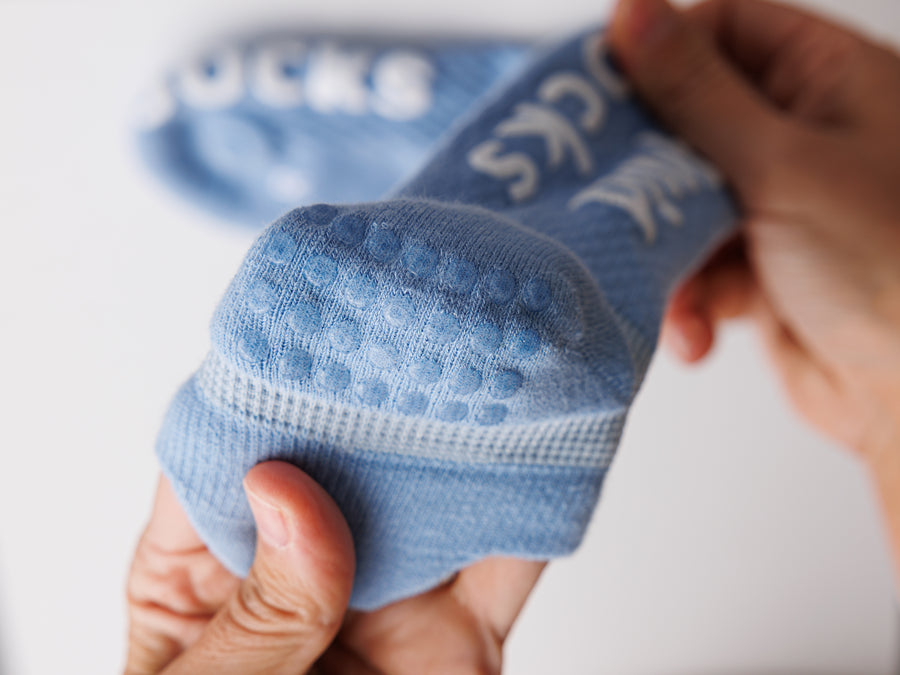 Hands holding a blue ankle sock to show rows of grip dots on the heel. By Squid Socks.