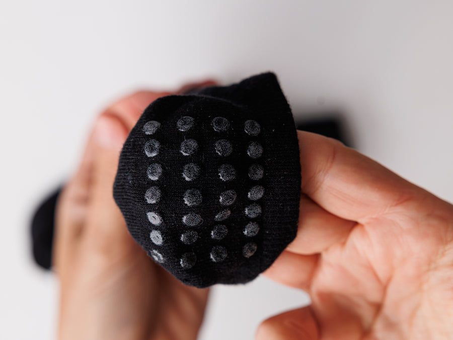 Hands holding a black sock heel close to the camera to show rows of grip dots. By Squid Socks.