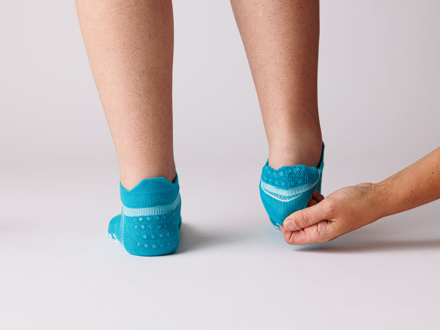 Person pulling back a turquoise ankle sock to show the grip dots inside the heel. By Squid Socks.