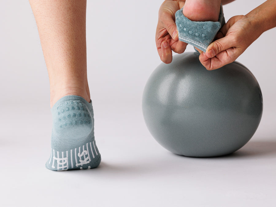 Person stretching one foot in teal no-show grip socks, with the sole and heel grips visible. By Squid Socks.