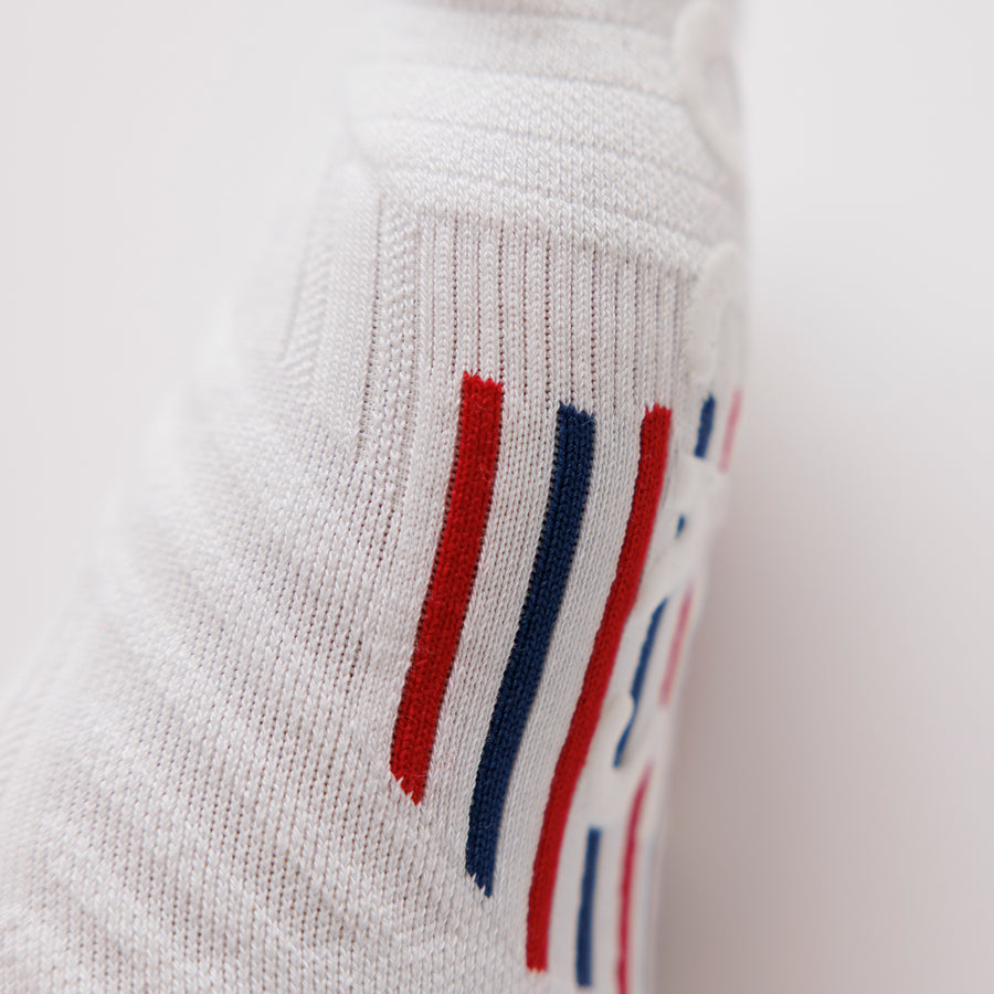 Close-up of a white no-show sock showing red and navy striped bottom grips. By Squid Socks.