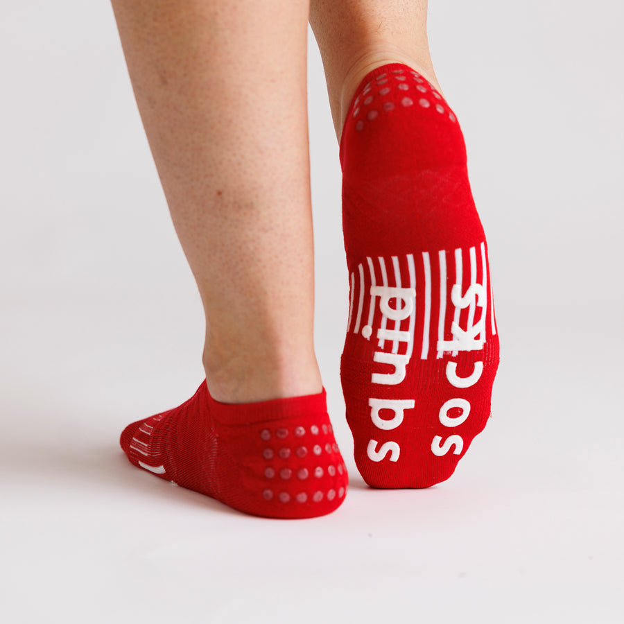 Red no-show grip socks viewed from behind, with one sole raised to show white bottom grips. By Squid Socks.