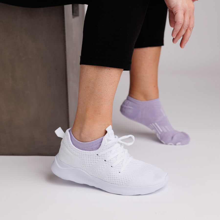 Lavender no-show grip socks worn with one white sneaker and one socked foot visible. By Squid Socks.