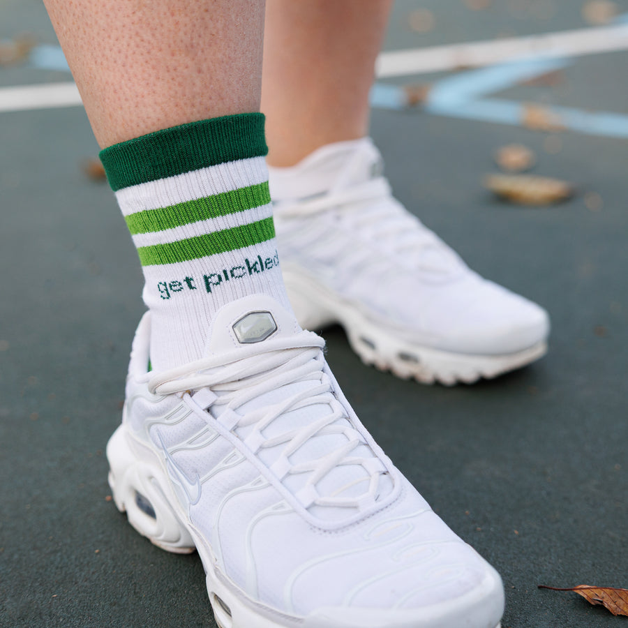 White and green striped crew pickleball grip socks with 'get pickled' lettering worn with white sneakers on a court. By Squid Socks.
