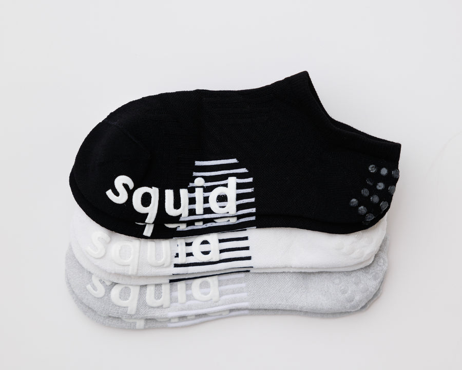 Back to Basics no-show grip socks in black, white, and gray, stacked with bottom and heel grips visible. By Squid Socks.