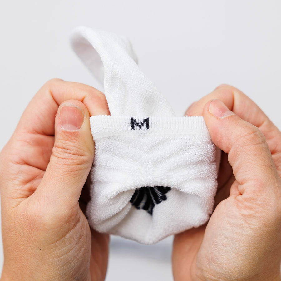 Hands opening a white no-show sock to show the size marking and interior heel. By Squid Socks.