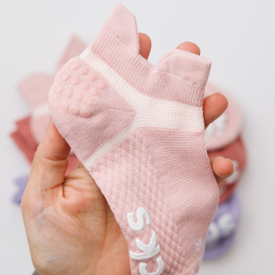 Hand holding a light pink ankle grip sock to show its heel and contrasting knit panels. By Squid Socks.