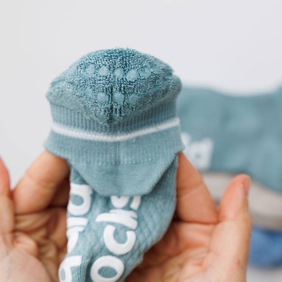 Close-up of a teal ankle sock heel held in both hands, showing rows of grip dots. By Squid Socks.