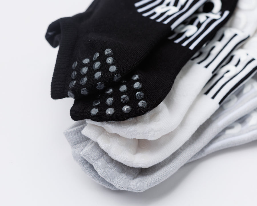 Close-up of stacked black, white, and gray no-show socks, with heel grip dots visible on the black sock. By Squid Socks.