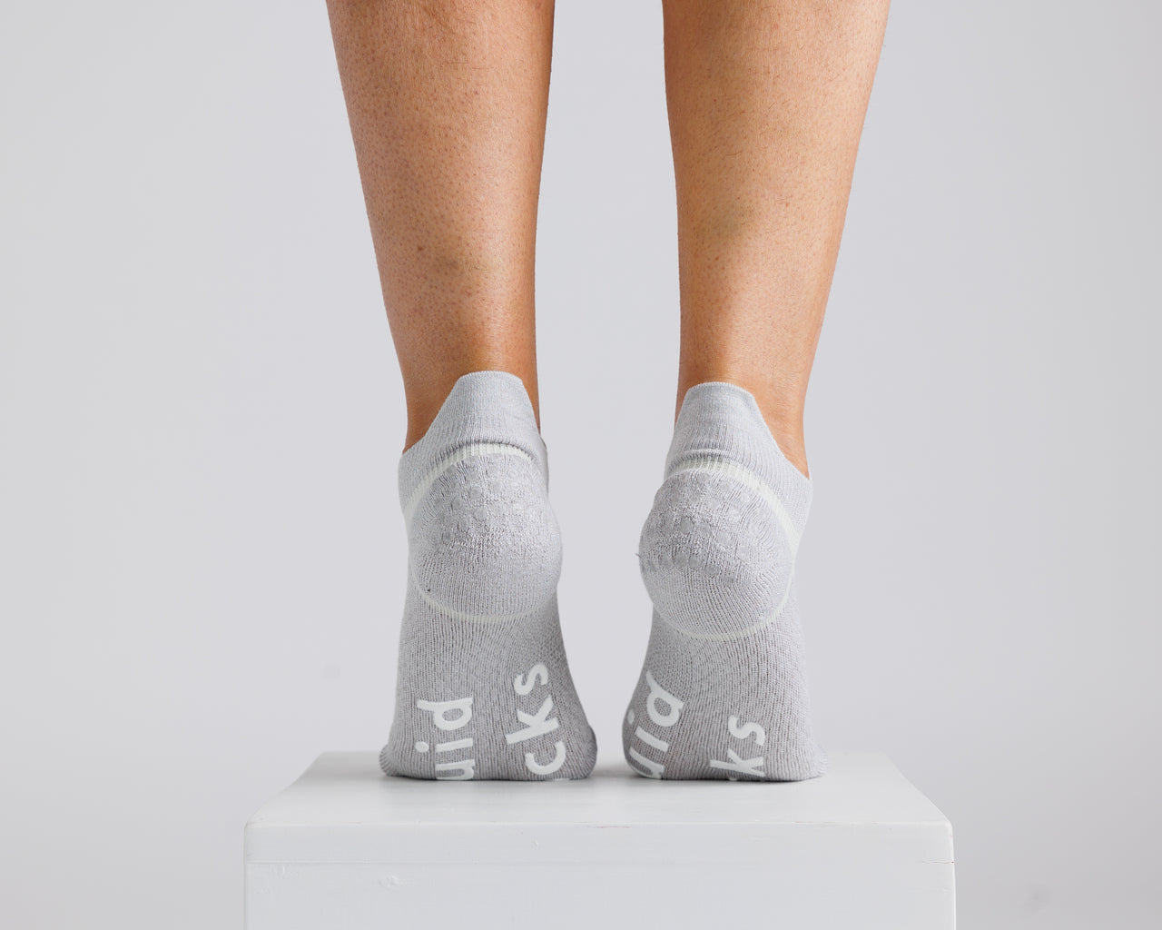 Gray ankle grip socks viewed from behind on a display block, showing heel and bottom grips. By Squid Socks.