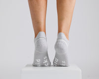 Thumbnail for Gray ankle grip socks viewed from behind on a display block, showing heel and bottom grips. By Squid Socks.