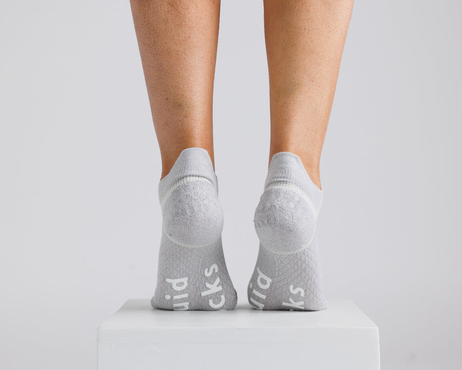 Gray ankle grip socks viewed from behind on a display block, showing heel and bottom grips. By Squid Socks.