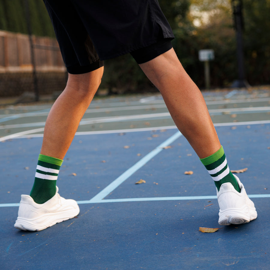 Person wearing green striped crew pickleball grip socks and white sneakers on an outdoor court. By Squid Socks.