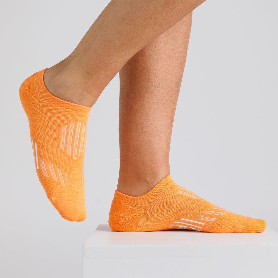 Orange no-show grip socks worn on a display block, showing side and top views. By Squid Socks.